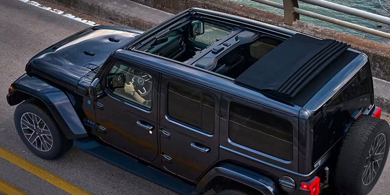 Overhead view of a black Jeep with its retractable soft top folded back, parked on a road beside water.