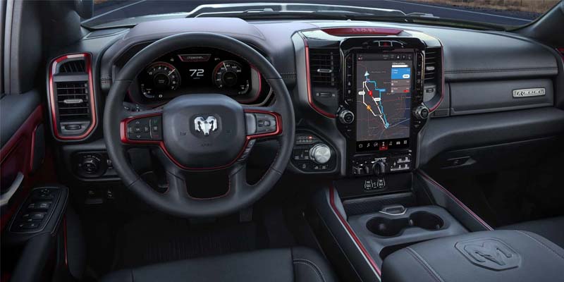 Interior of a Ram truck with black and red accents, large central touchscreen navigation, and a digital instrument cluster.