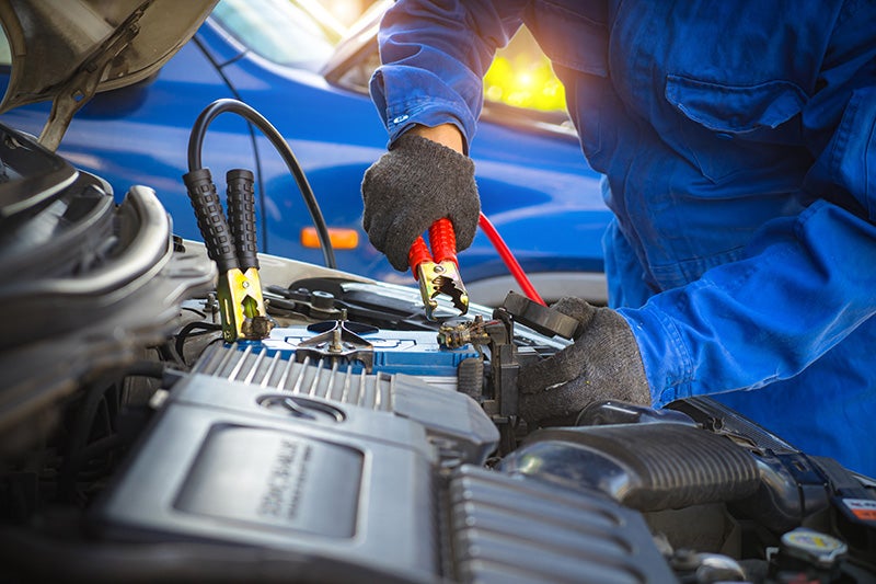 Technician attaching jumper cables to vehicle battery under hood